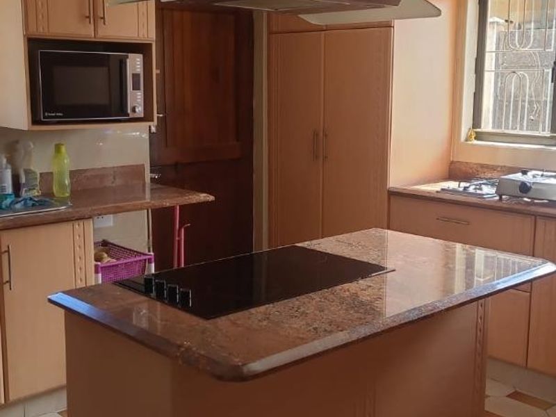 A functional kitchen featuring wooden cabinetry, granite countertops, a central island with an induction cooktop, and a stainless steel extractor fan.