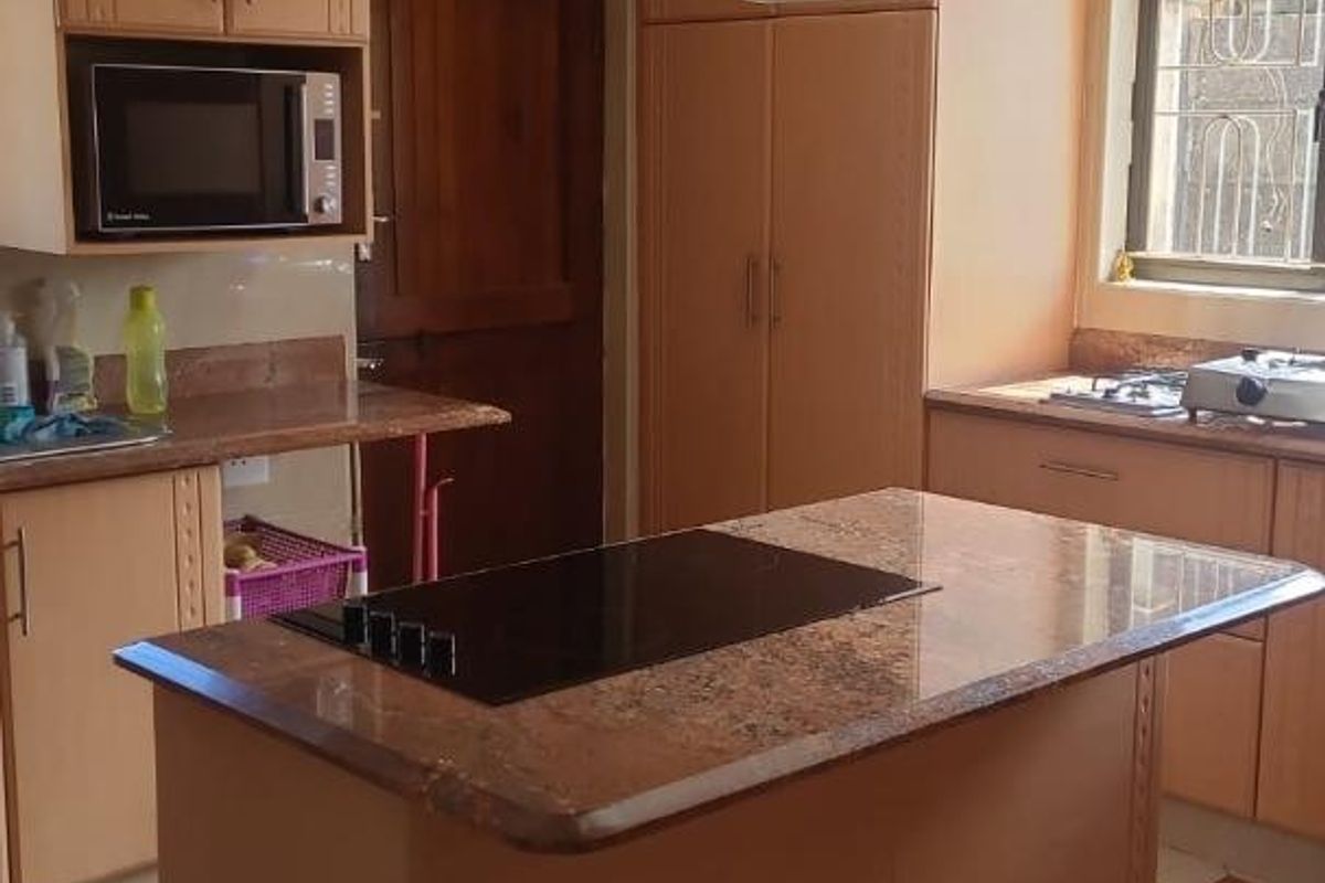 A functional kitchen featuring wooden cabinetry, granite countertops, a central island with an induction cooktop, and a stainless steel extractor fan.
