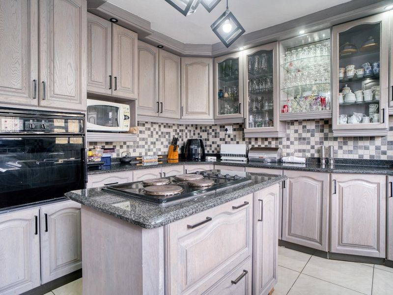 A well-appointed kitchen featuring granite countertops, a central island with a built-in hob, integrated oven, and ample glass-fronted cabinetry for display storage.