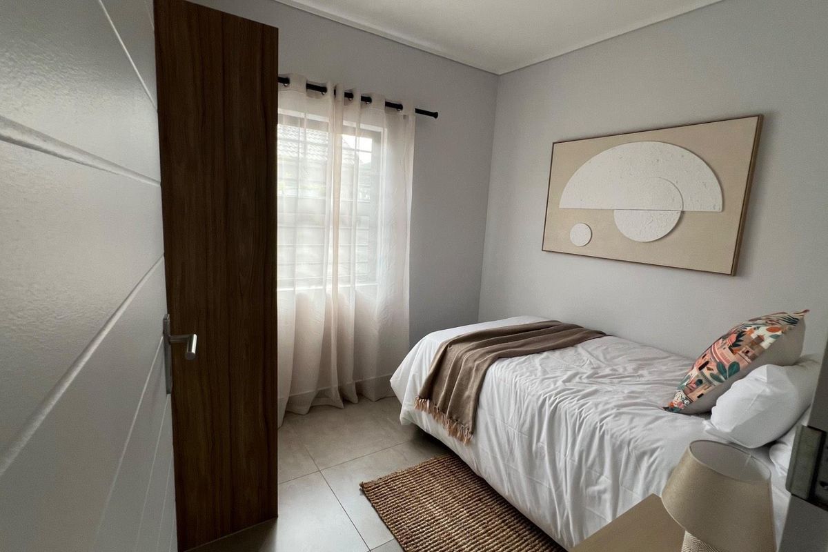 A compact, well-maintained bedroom featuring neutral wall tones, tiled flooring, and a window with natural light.