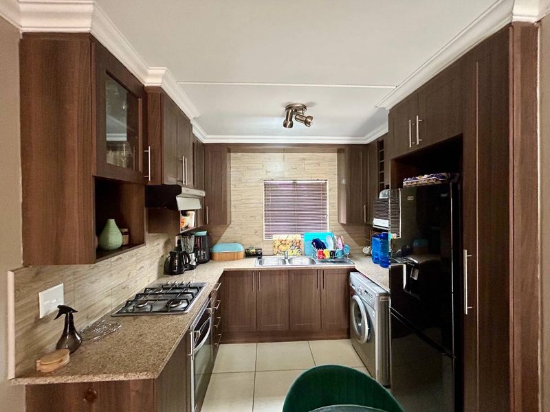 A functional kitchen featuring dark wood cabinetry, granite countertops, a gas hob, an under-counter oven, and space for a washing machine.