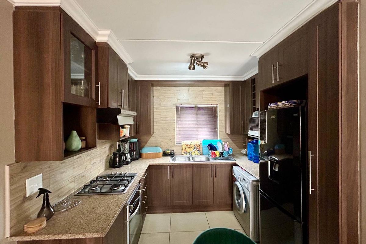 A functional kitchen featuring dark wood cabinetry, granite countertops, a gas hob, an under-counter oven, and space for a washing machine.
