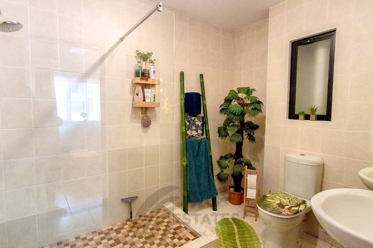 A functional bathroom featuring a walk-in shower with glass screen, dual vanity basins, and a standard toilet with neutral wall tiling.