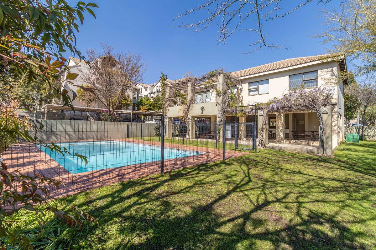 Rear view of the apartment complex featuring a private swimming pool, covered patio area with pergola, and a well-maintained garden lawn.