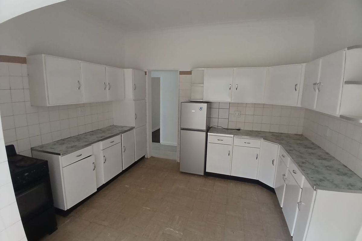 Functional kitchen featuring white cabinetry, laminate countertops, tiled splashbacks, and space for a freestanding stove and refrigerator.