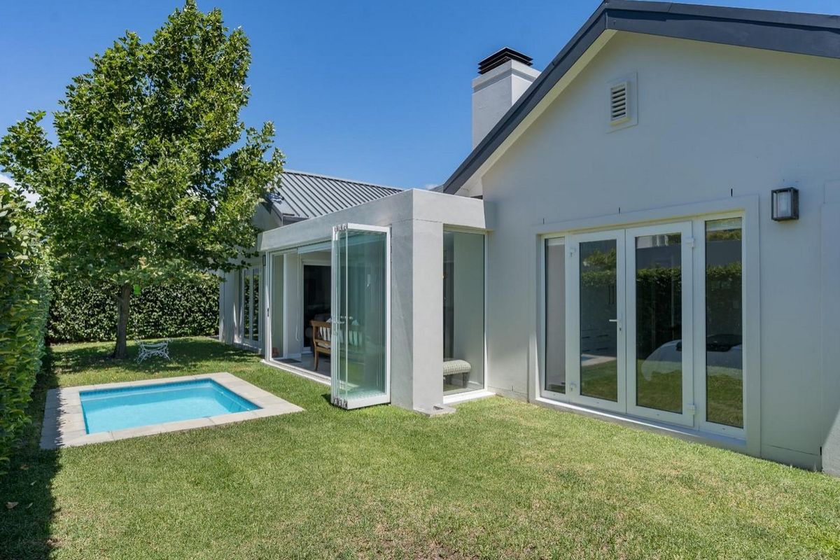 Rear view of the property featuring a manicured lawn, a small plunge pool, and modern glass stacker doors leading into the living area.