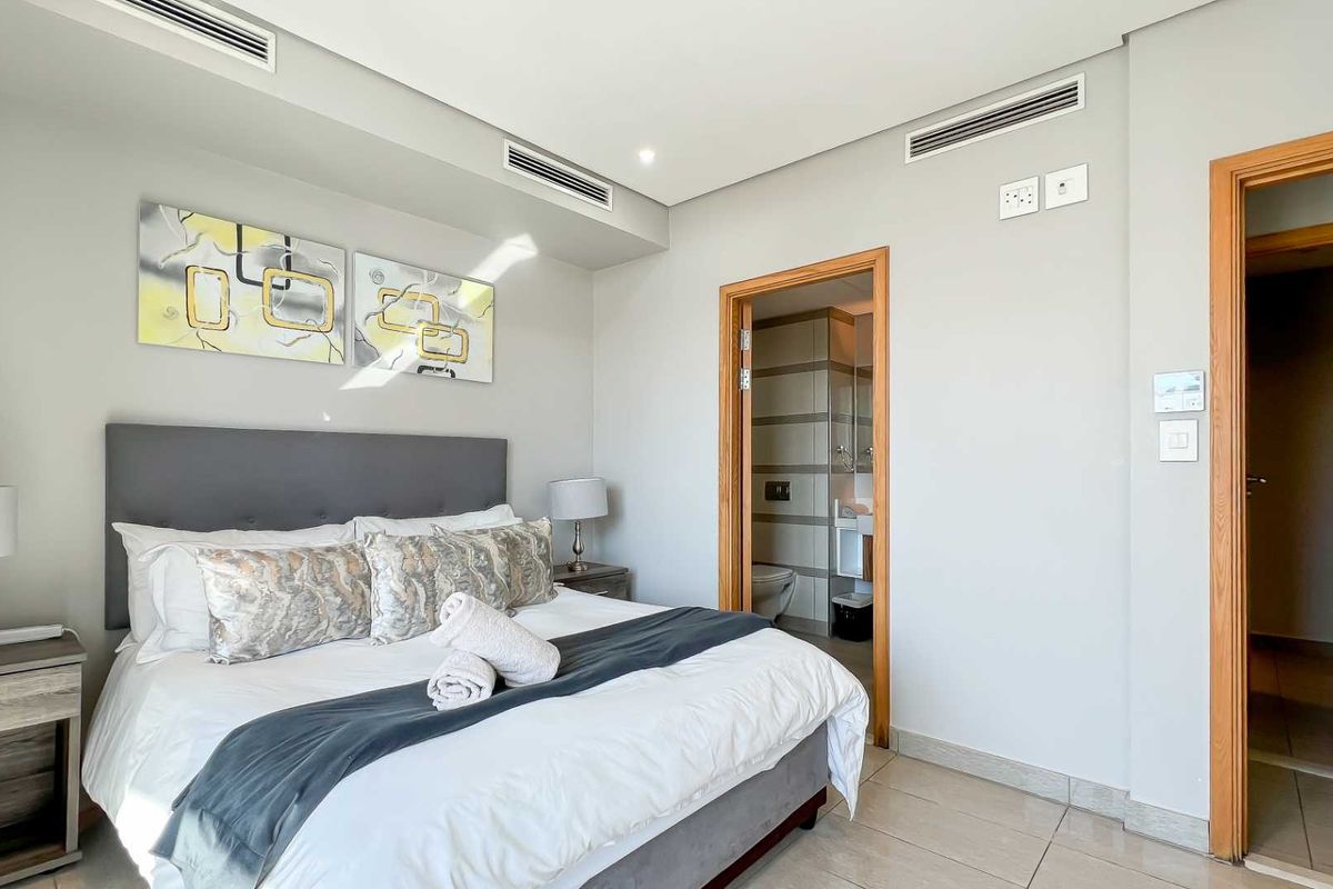 A well-maintained bedroom featuring tiled flooring, recessed ceiling lighting, ducted air conditioning, and an en-suite bathroom.