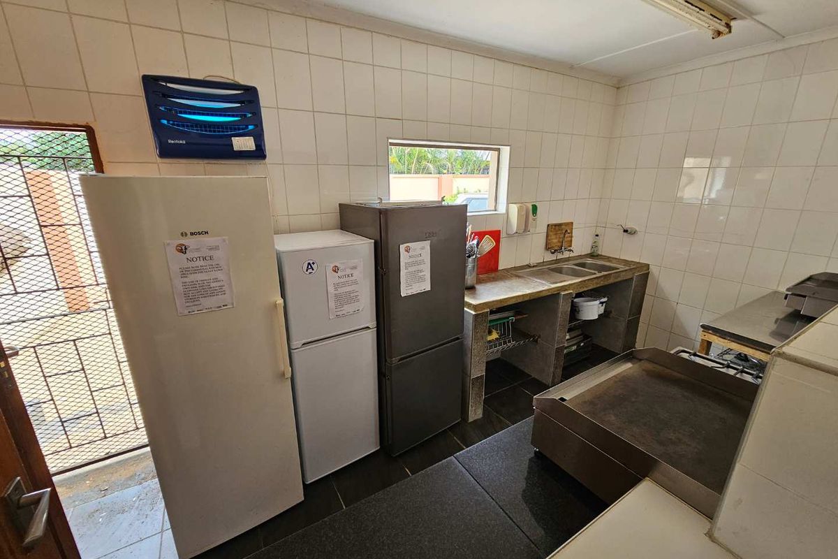 A functional commercial-style kitchen area featuring tiled walls, stainless steel prep surfaces, double sink, and multiple refrigeration units.