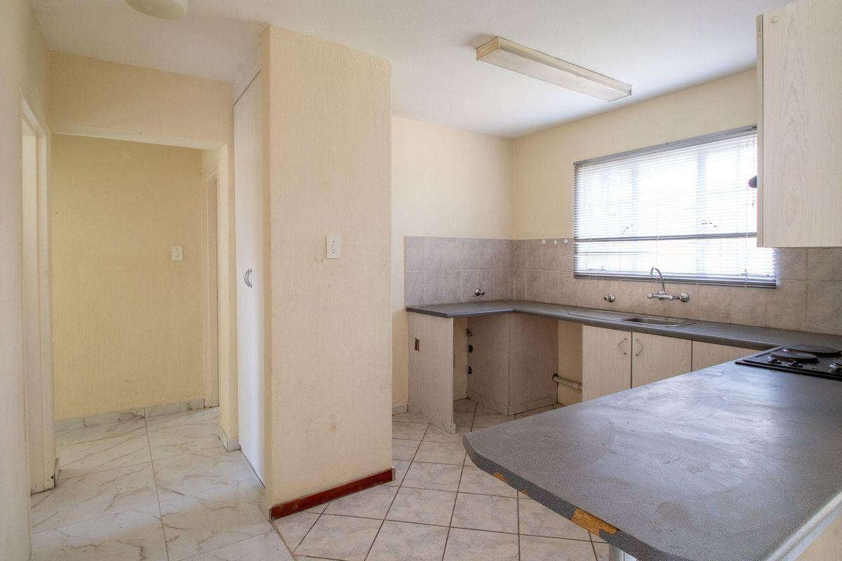 A dated kitchen featuring tiled flooring, laminate countertops, built-in cabinetry, and a fitted hob, offering a functional layout ready for modernization.