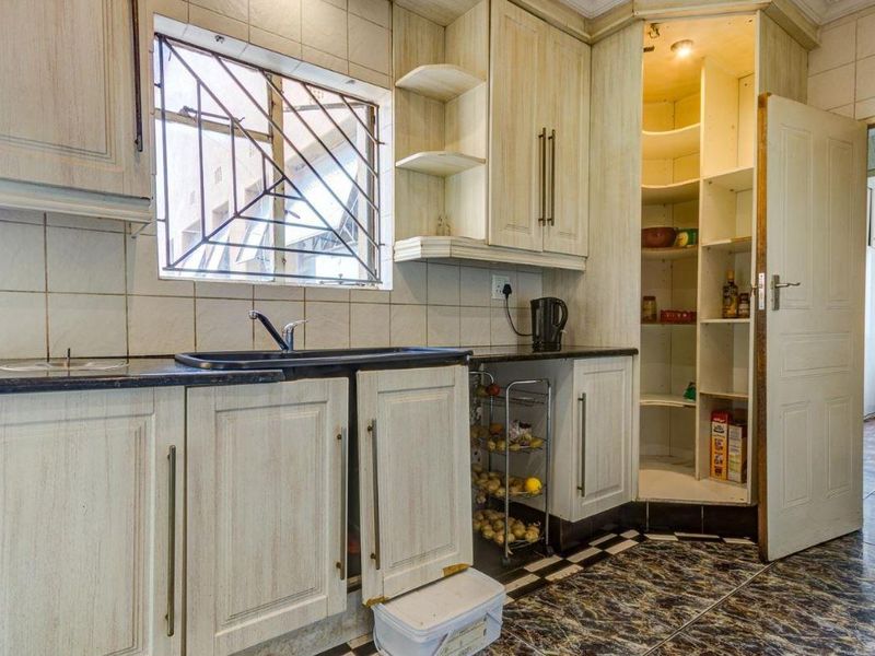A dated kitchen featuring built-in cabinetry, laminate countertops, a double sink, and a built-in pantry with tiled flooring and backsplash.