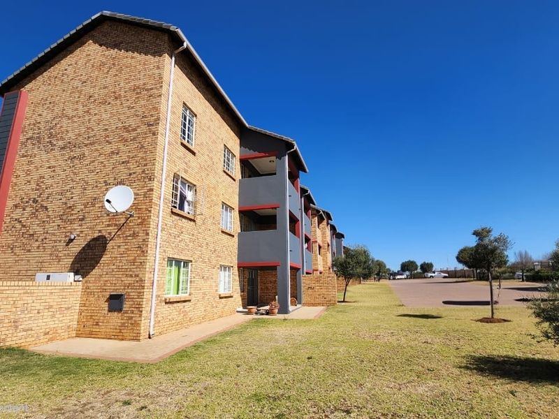 A view of the rear elevation of a multi-story apartment complex featuring face brick construction, private balconies, and surrounding landscaped grounds.