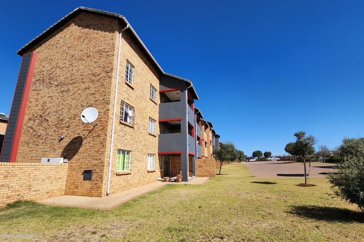 A view of the rear elevation of a multi-story apartment complex featuring face brick construction, private balconies, and surrounding landscaped grounds.