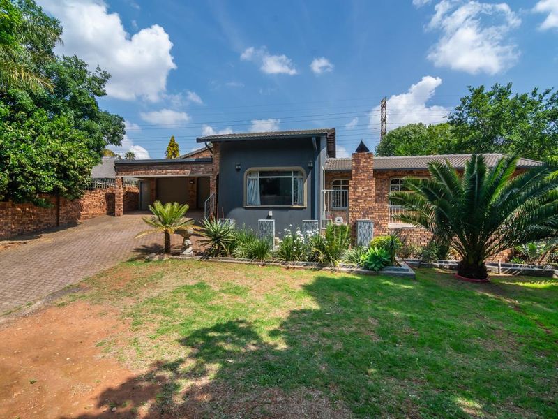 A well-maintained single-story face brick house featuring a paved driveway, covered carport, and established front garden.