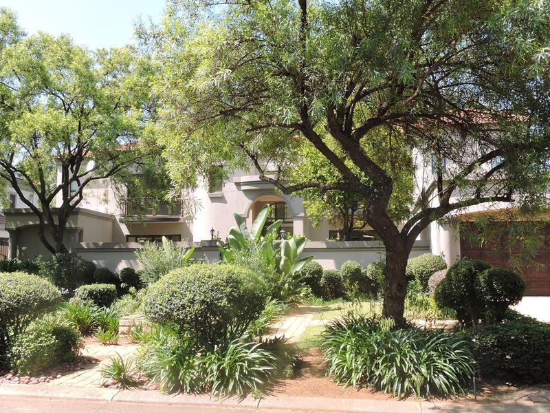 Front elevation of a residential property featuring a paved driveway, double garage, and established landscaped garden with mature trees.