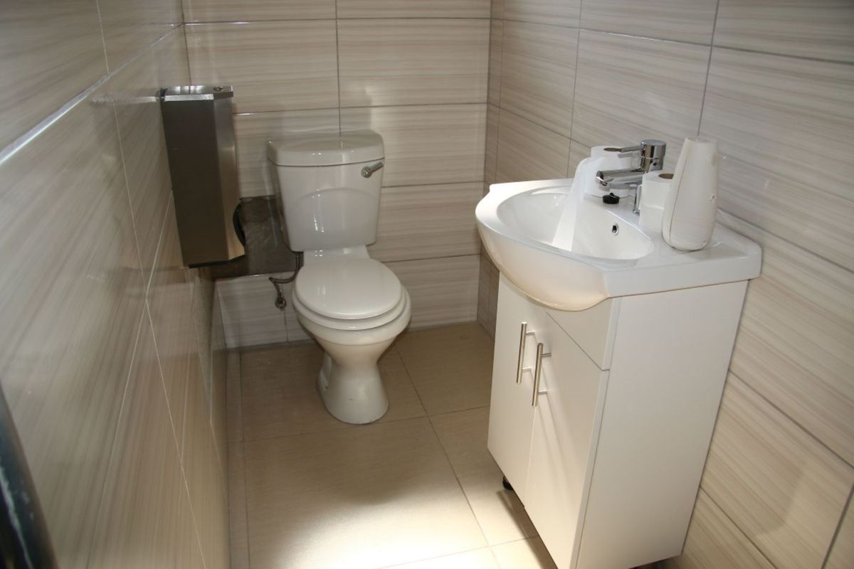 A clean, functional bathroom featuring tiled walls and flooring, a white vanity cabinet with a basin, and a standard toilet.
