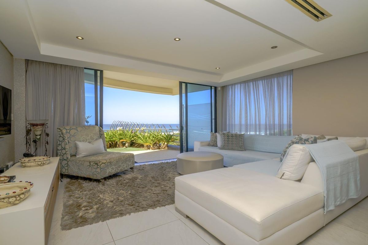 Spacious living room featuring tiled floors, recessed lighting, and large sliding glass doors opening onto a balcony with ocean views.