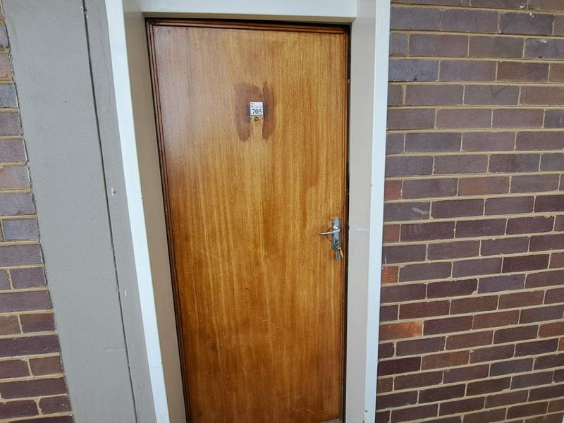 Exterior view of an apartment entrance door featuring a timber veneer finish set within a brick facade.