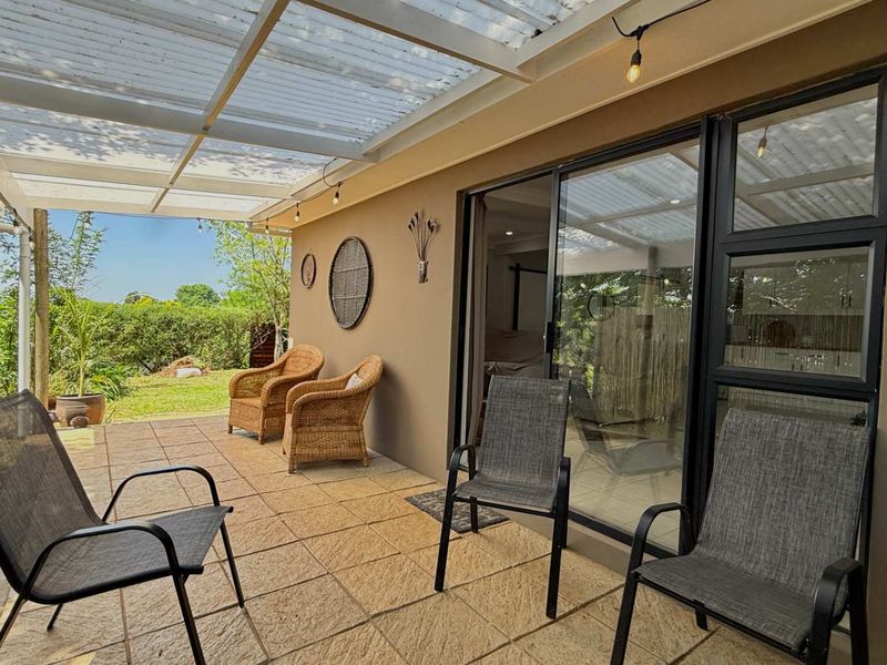 A covered outdoor patio featuring tiled flooring, timber support posts, and sliding glass doors providing access to the interior living space.