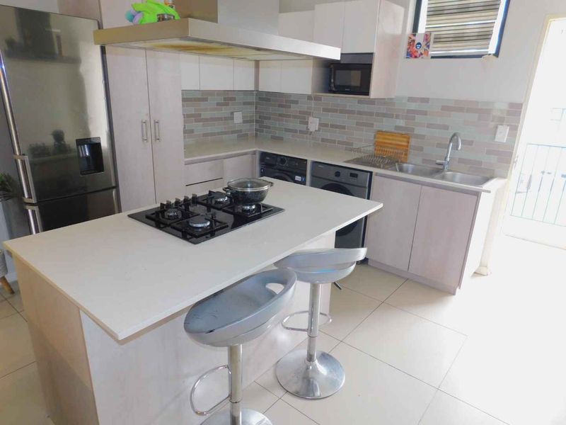 Modern kitchen featuring a central island with a gas hob, extractor fan, built-in cabinetry, and a double sink with a tiled backsplash.