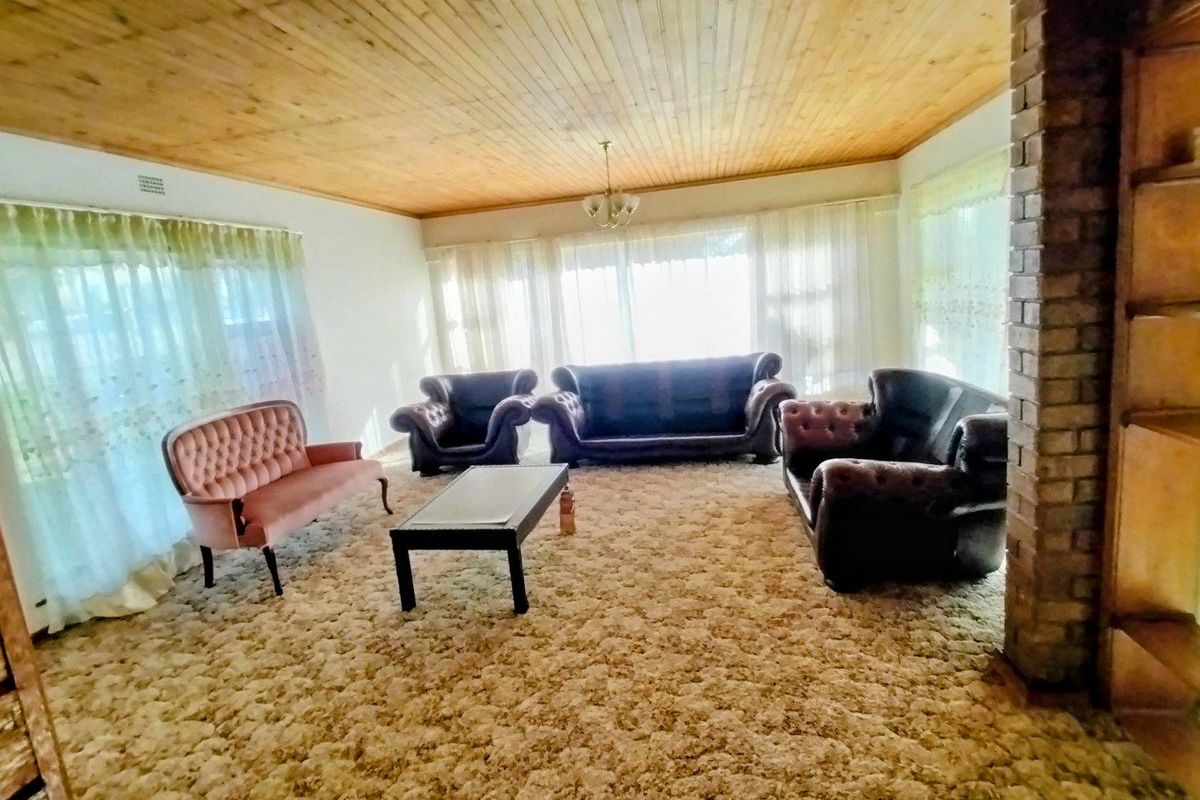 Spacious living room featuring a timber tongue and groove ceiling, exposed brick pillar, and wall-to-wall carpeting, offering a dated aesthetic ready for modernization.