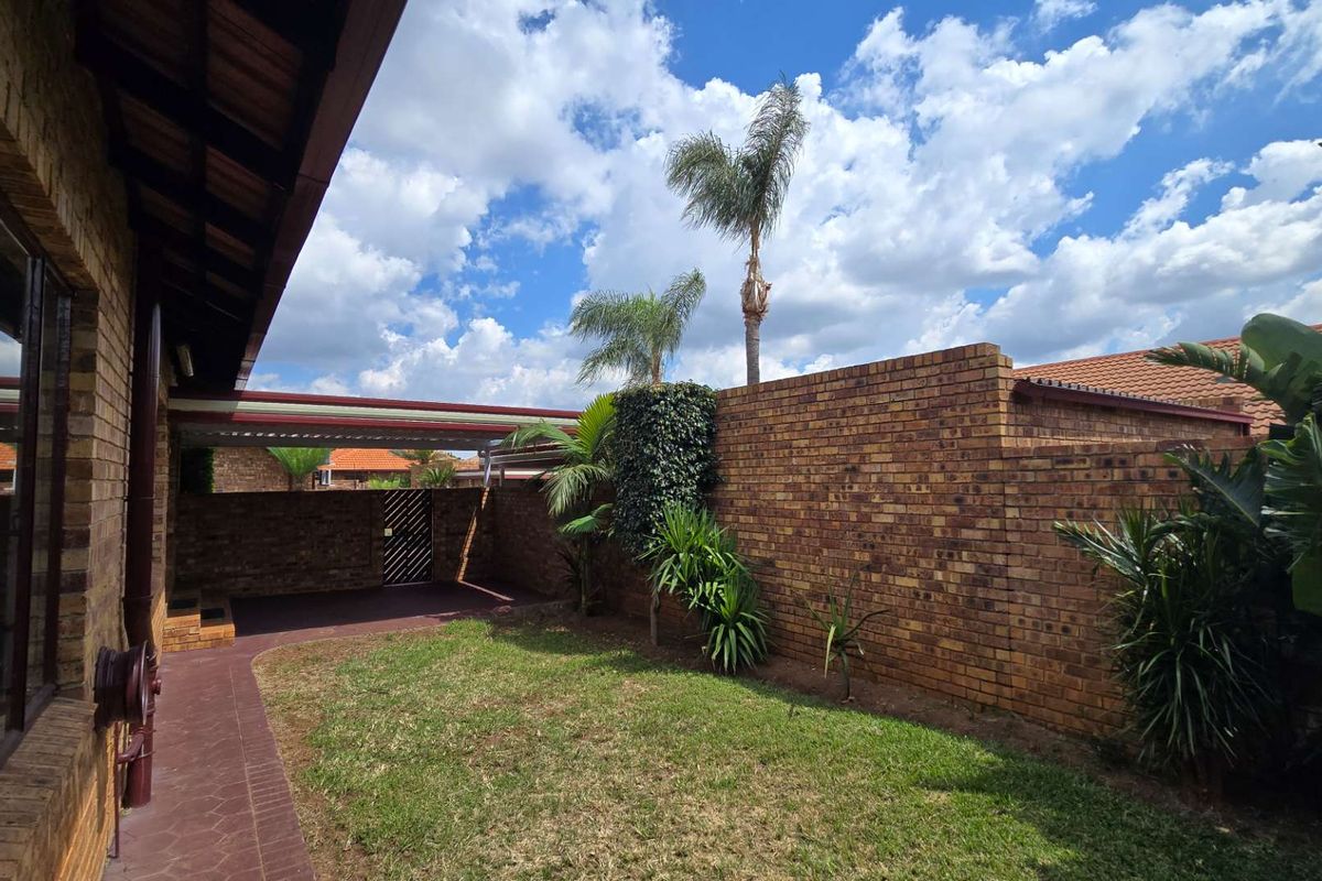 A private rear garden area featuring a brick boundary wall, paved walkway, and a covered carport structure.