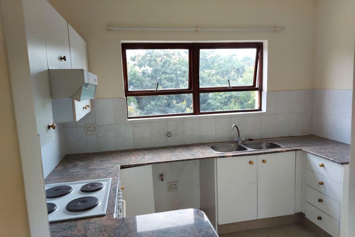 A functional kitchen featuring granite countertops, built-in cabinetry, an electric hob with extractor fan, and a double basin sink with a garden view.