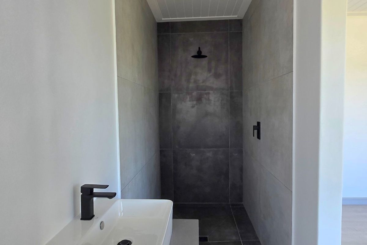 A modern, minimalist bathroom featuring a walk-in shower with dark grey tiling, a sleek basin, and contemporary black fixtures.