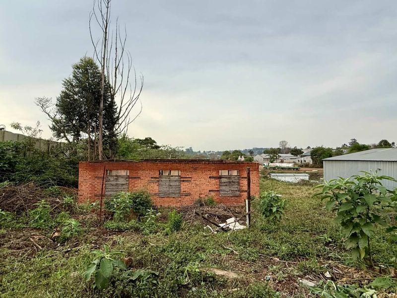 A view of a derelict brick structure on a vacant commercial plot, featuring boarded windows and overgrown grounds, suitable for redevelopment.