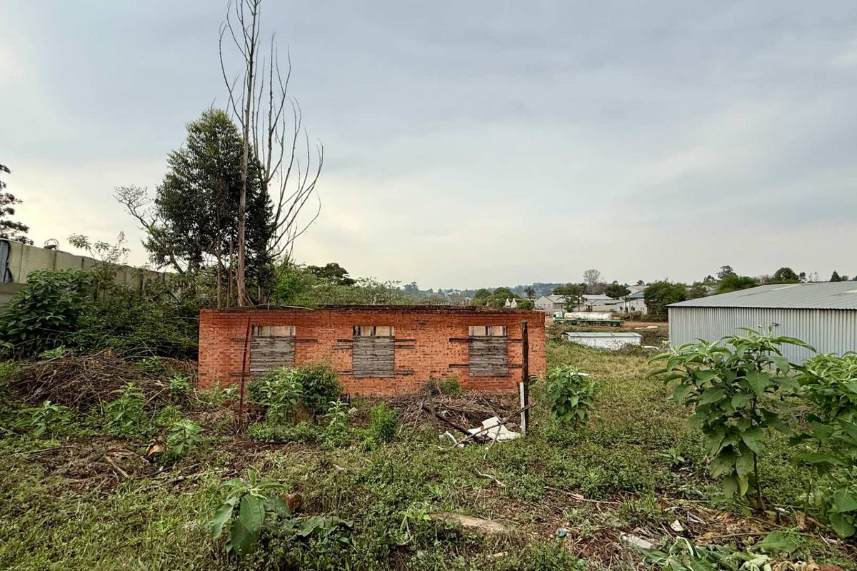 A view of a derelict brick structure on a vacant commercial plot, featuring boarded windows and overgrown grounds, suitable for redevelopment.