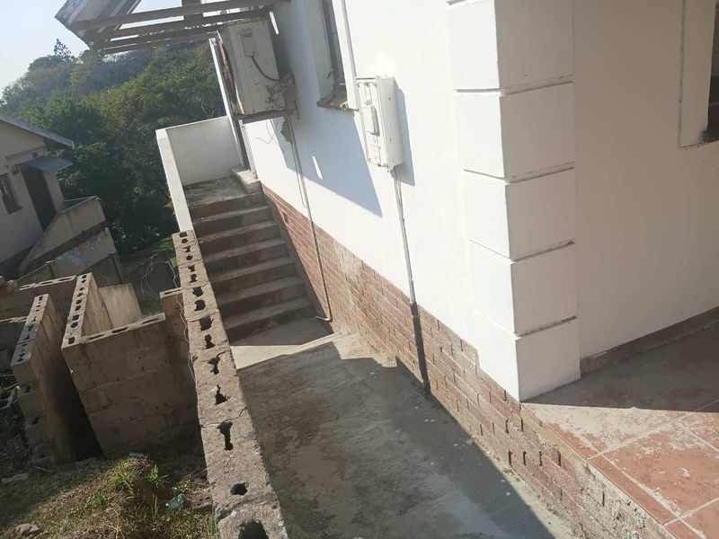 Exterior view of the rear property showing a concrete staircase, brick masonry wall, and utility installations.