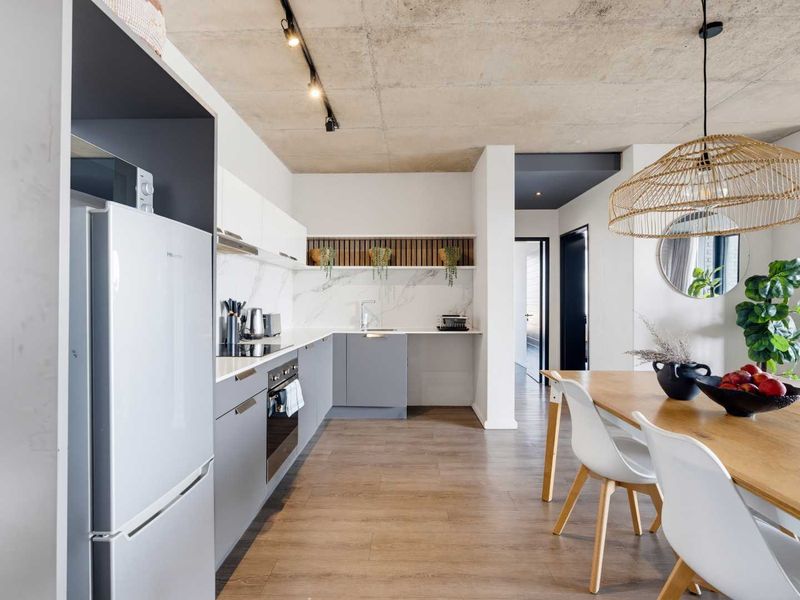 Modern open-plan kitchen and dining area featuring an exposed concrete ceiling, sleek cabinetry, marble-look splashback, and high-quality finishes throughout.