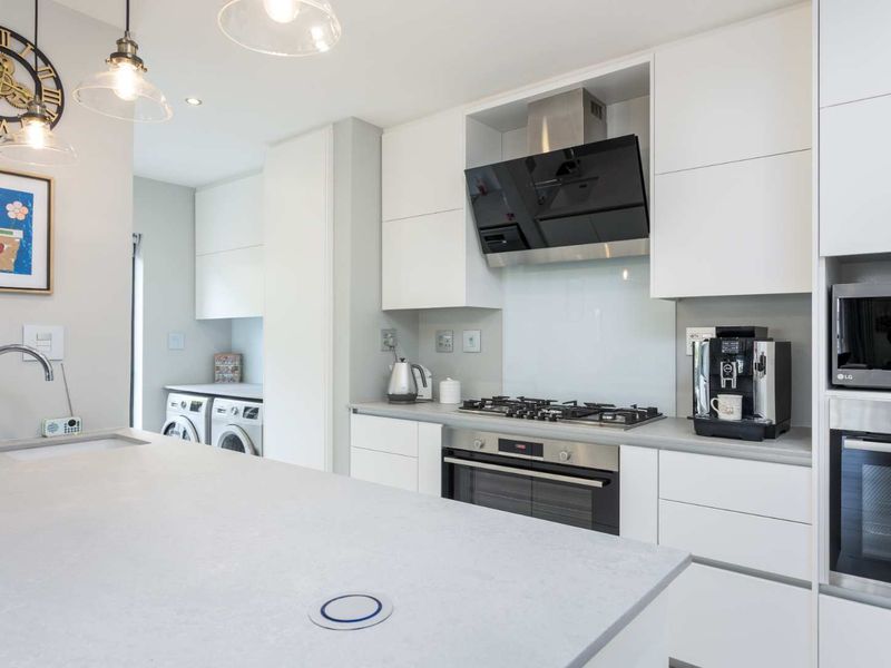 Modern kitchen featuring a large island, stone countertops, built-in appliances, and a sleek white cabinetry finish with an adjacent laundry area.