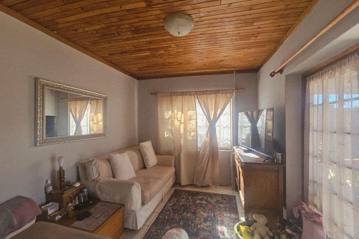 A cozy living room featuring a distinctive timber-paneled ceiling, tiled flooring, and natural light through a window and glass door.