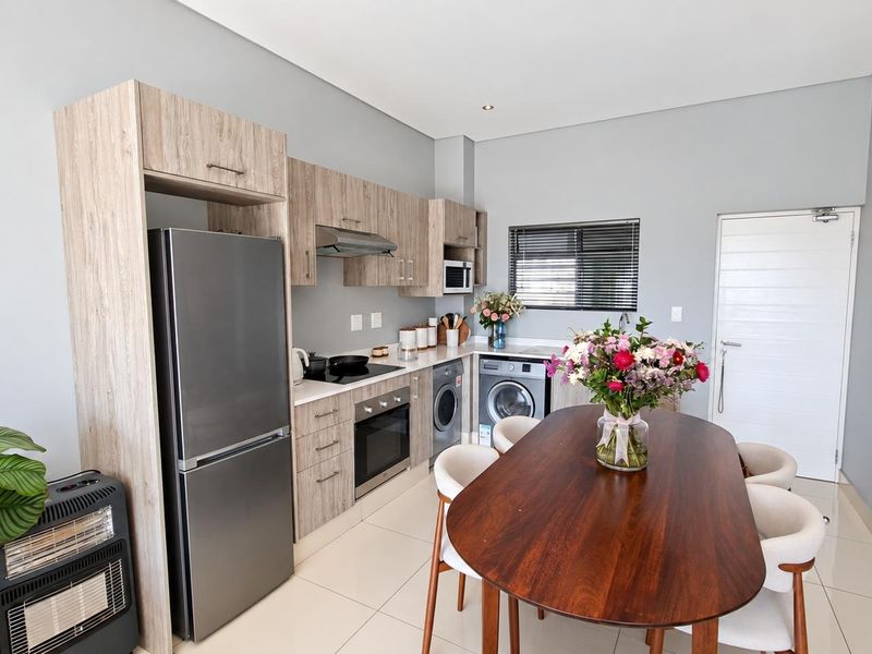 Modern open-plan kitchen featuring light wood cabinetry, integrated appliances, and sleek tiled flooring, seamlessly flowing into the dining area.