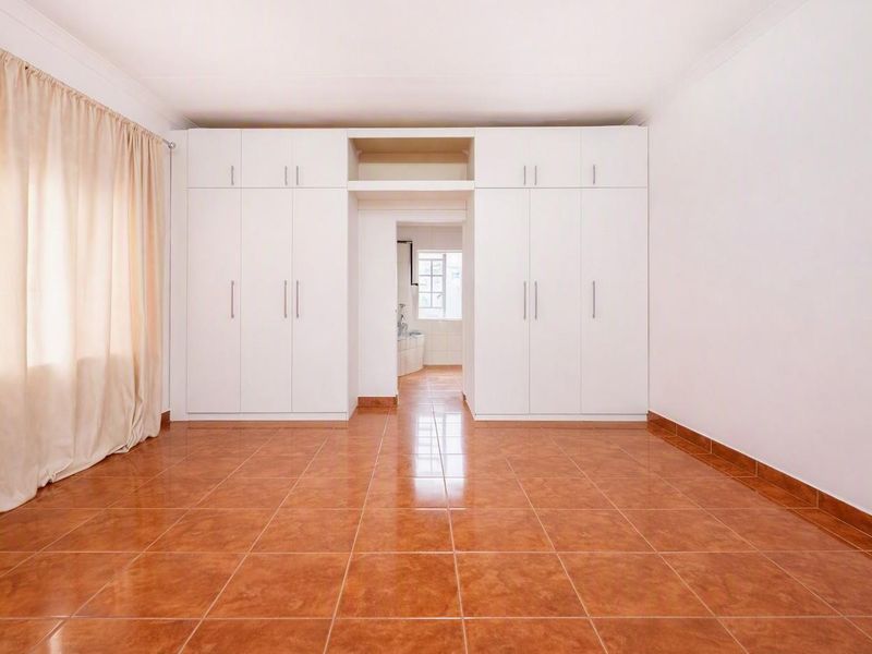 A spacious, empty bedroom featuring neutral white built-in cupboards, tiled flooring, and a coved ceiling, offering a clean and versatile living space.