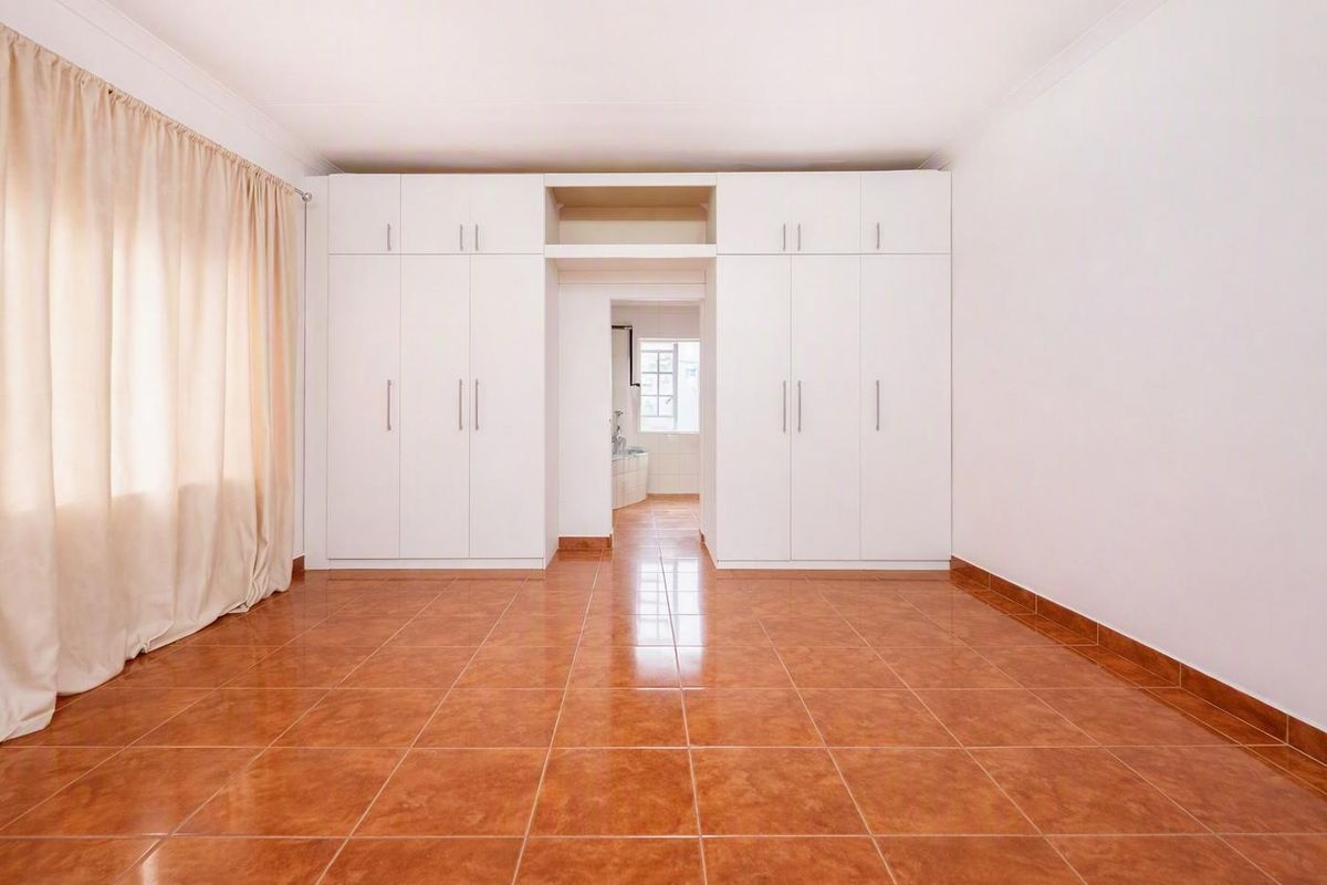 A spacious, empty bedroom featuring neutral white built-in cupboards, tiled flooring, and a coved ceiling, offering a clean and versatile living space.