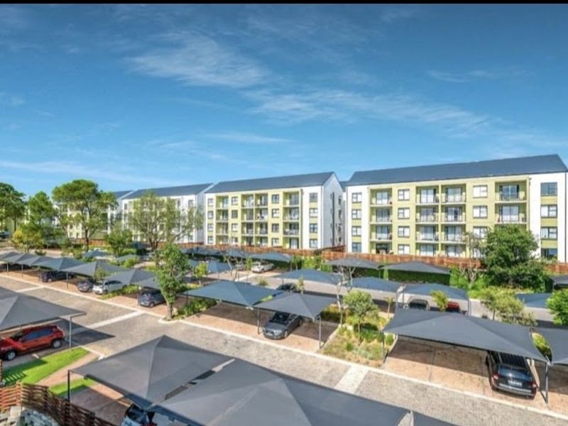 Exterior view of a modern multi-story apartment complex featuring extensive covered parking bays and well-maintained landscaped grounds.