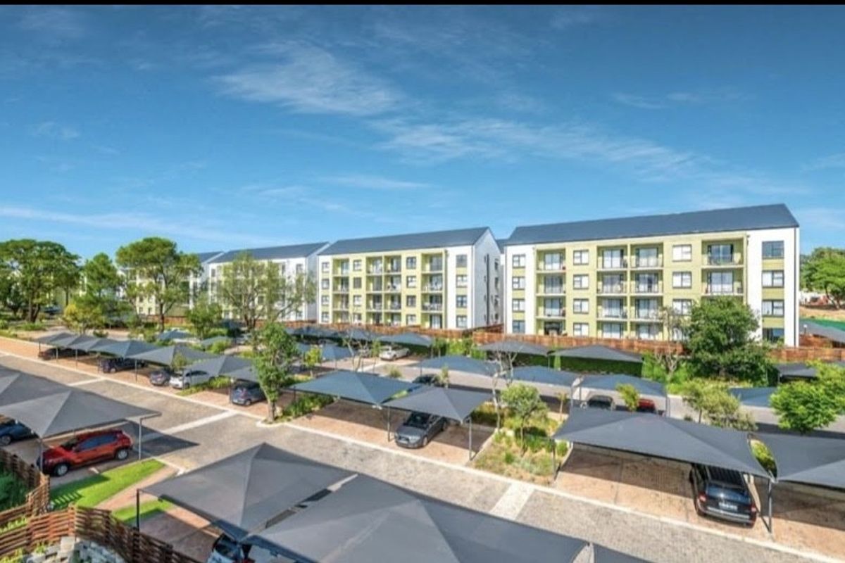 Exterior view of a modern multi-story apartment complex featuring extensive covered parking bays and well-maintained landscaped grounds.