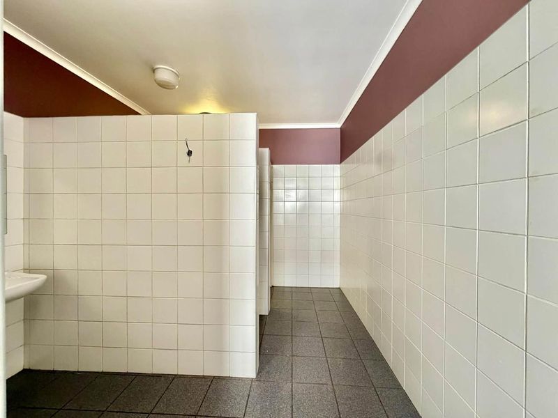 A functional, tiled commercial bathroom facility featuring partition walls and neutral floor tiling, presenting a clean but dated aesthetic.