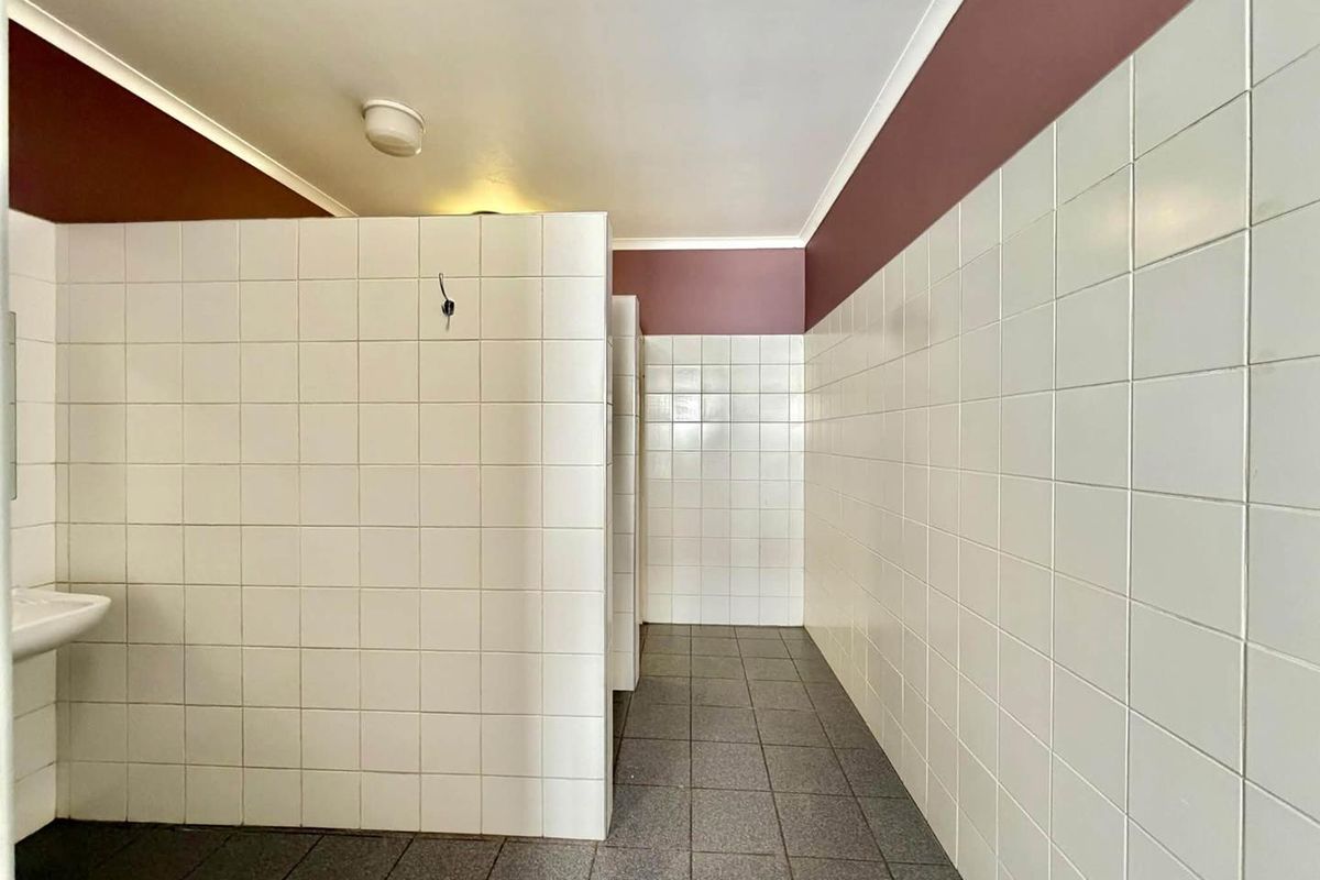 A functional, tiled commercial bathroom facility featuring partition walls and neutral floor tiling, presenting a clean but dated aesthetic.