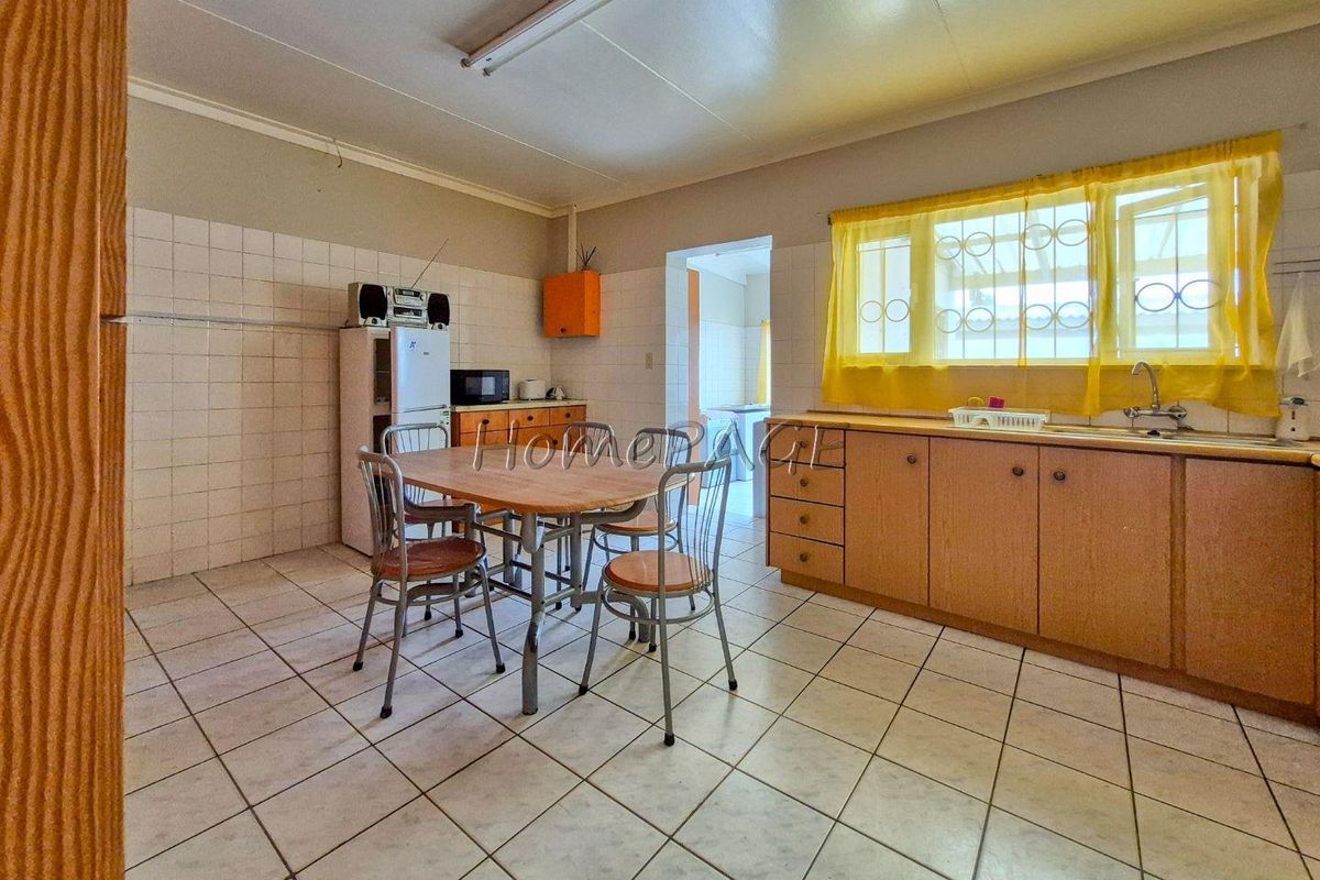 A functional kitchen featuring wooden cabinetry, tiled flooring, and a tiled splashback, offering a practical layout with potential for modernization.