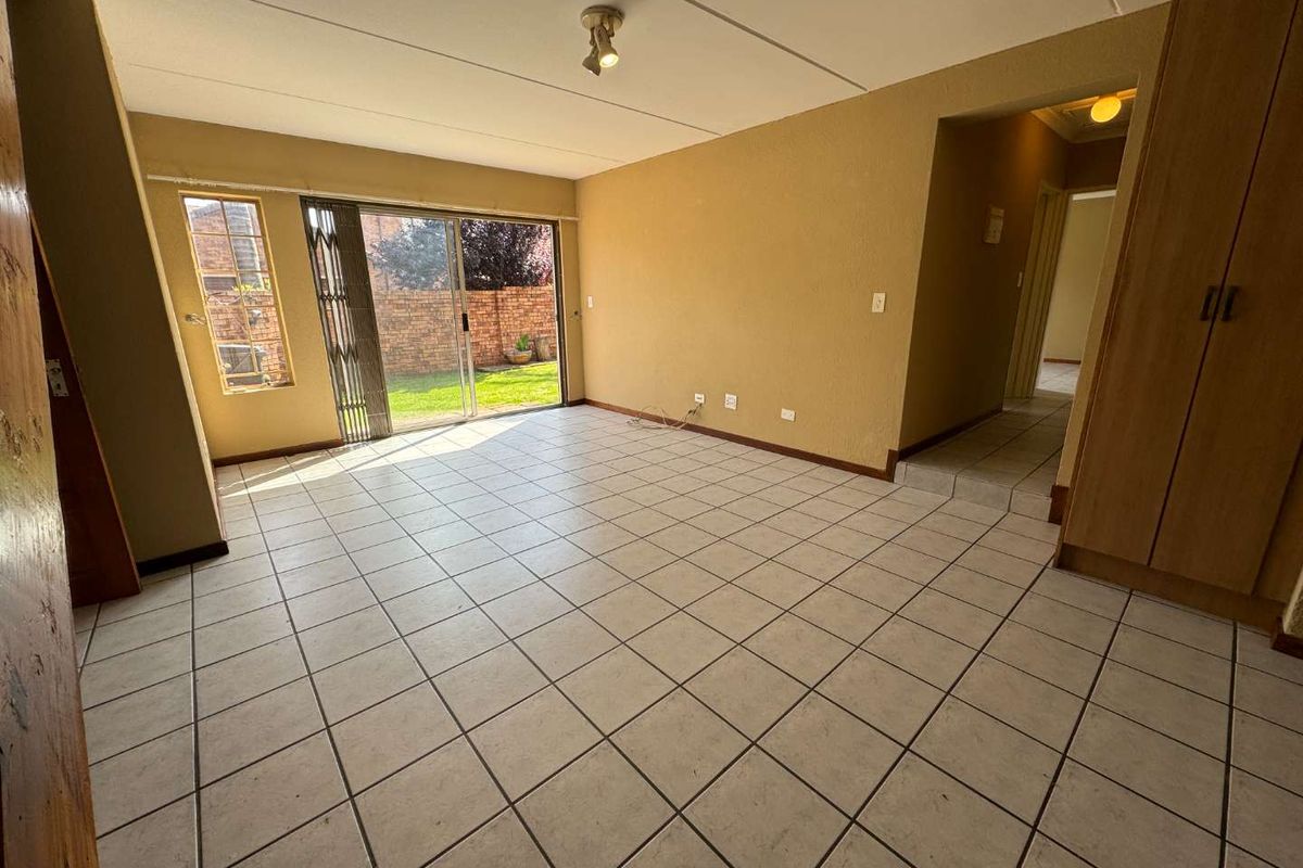 An empty living room featuring tiled flooring, a built-in cupboard, and a sliding glass door providing access to the rear garden.