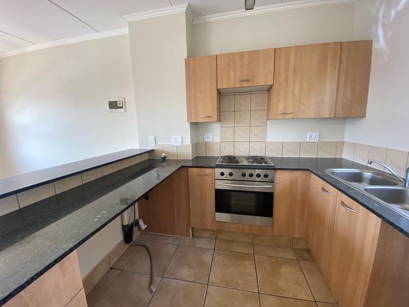 A functional kitchen featuring granite countertops, built-in cabinetry, an electric hob with oven, and a double stainless steel sink with tiled splashbacks.