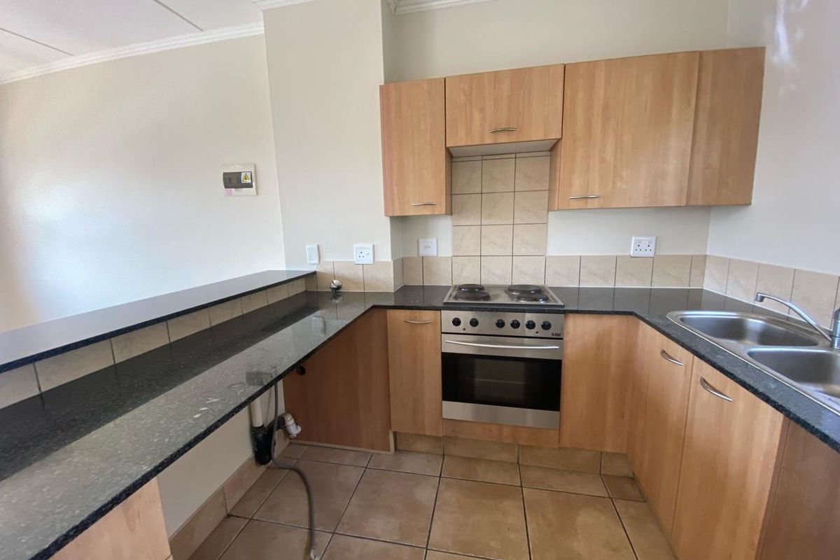 A functional kitchen featuring granite countertops, built-in cabinetry, an electric hob with oven, and a double stainless steel sink with tiled splashbacks.