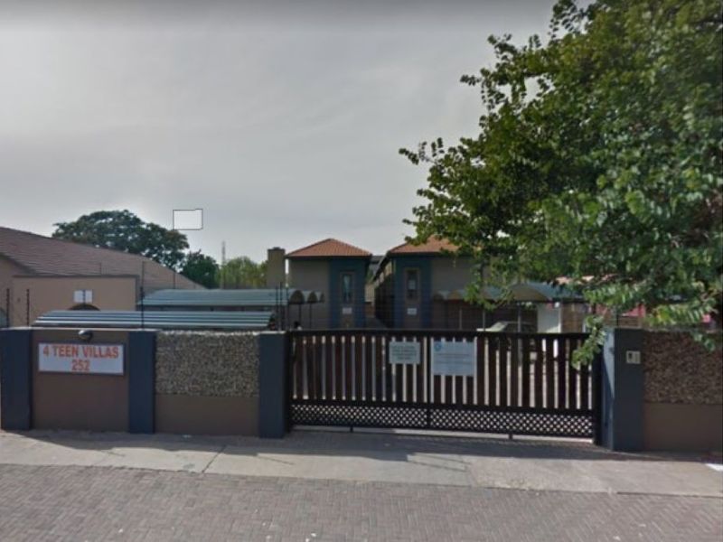 Street view of the front entrance to 4 Teen Villas, featuring a secure gated access point, perimeter wall with electric fencing, and paved driveway area.