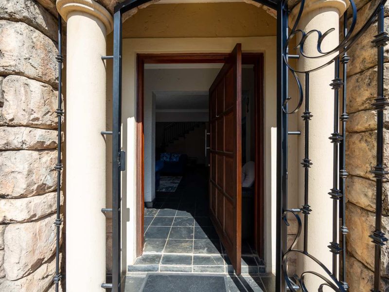 Main entrance featuring stone cladding, decorative columns, a wrought iron security gate, and a solid timber door opening onto slate flooring.