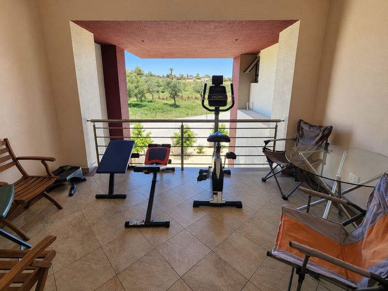 A covered balcony featuring tiled flooring, recessed lighting, and a stainless steel balustrade, offering an open view of the surrounding landscape.