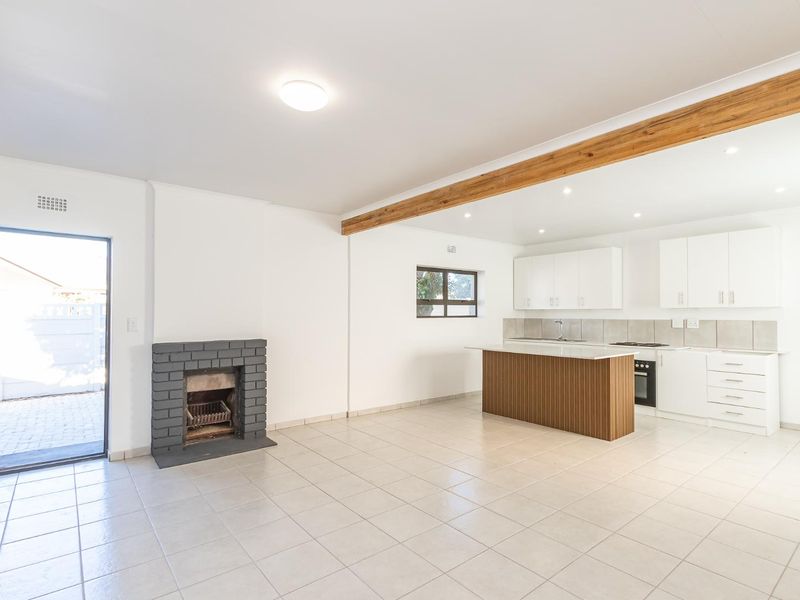Spacious open-plan living area featuring a brick fireplace, tiled flooring, and a modern kitchen with a central island and built-in appliances.