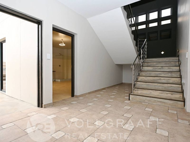Spacious entrance hall featuring a modern staircase with stainless steel balustrades and tiled flooring, leading to an adjacent room.
