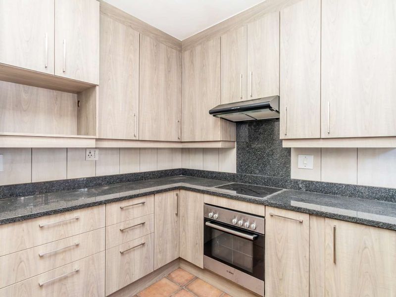 A clean, functional kitchen featuring light wood-finish cabinetry, dark granite countertops, a built-in oven, electric hob, and extractor fan with tiled backsplash.